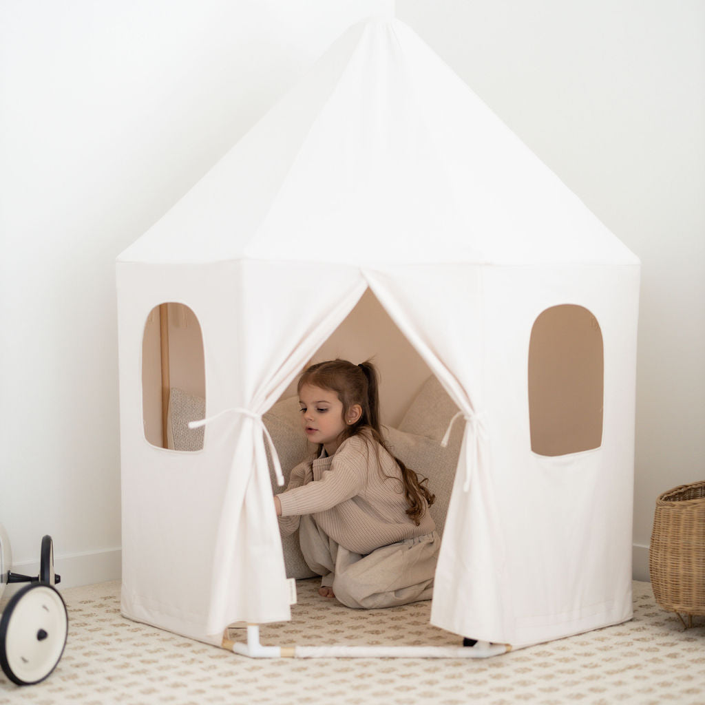 Child playing inside a white cotton pavilion play tent with two windows in a room.
