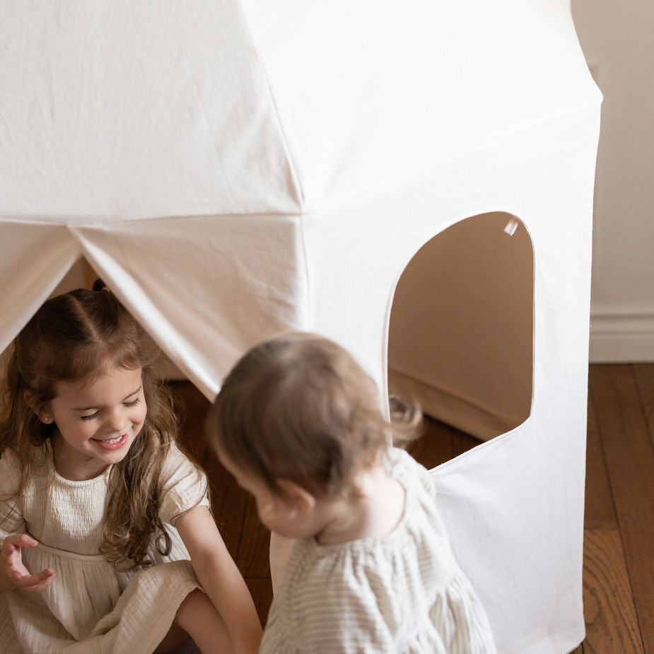 Child playing inside a white cotton pavilion play tent with two windows in a room.